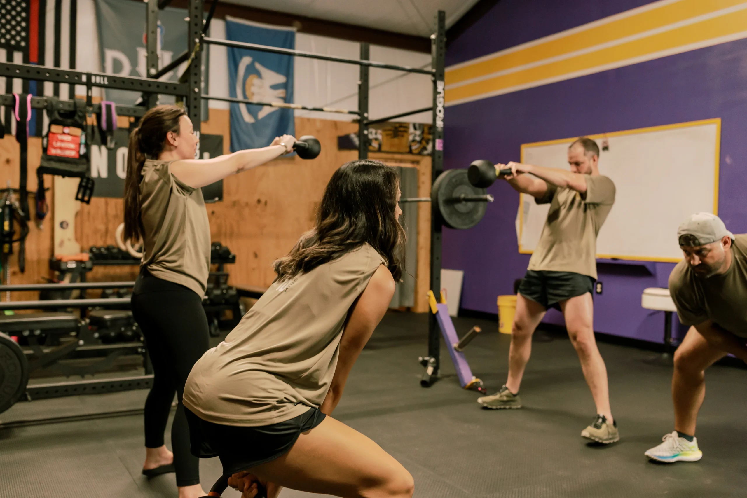 Group of people in a gym doing kettlebell swings, wearing matching workout attire.